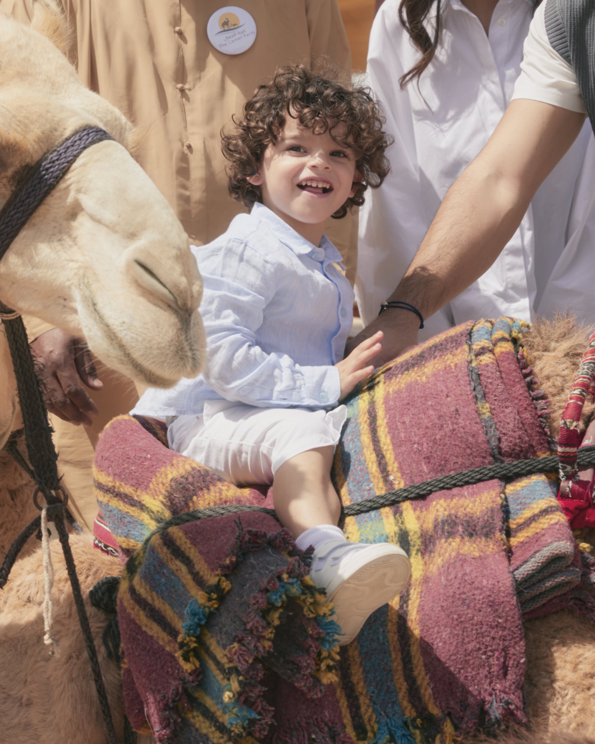 Aboudi smiling beside a camel at the Dubai desert camel farm
      — Emporio Armani campaign by Ali & Walaa, April 2024
