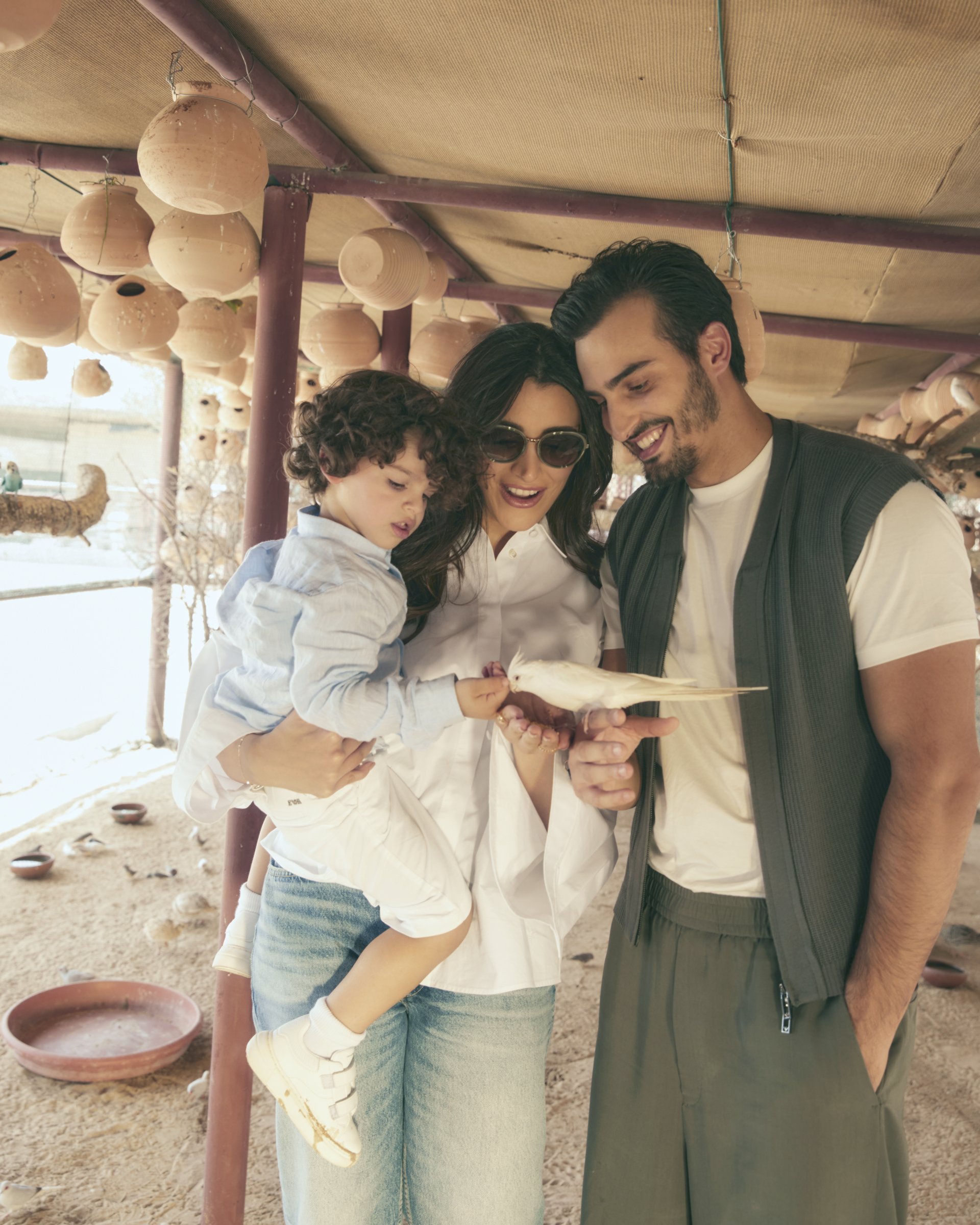 Ali, Walaa, and Aboudi feeding a small white bird under a
    canopy of hanging clay pots — Emporio Armani campaign by Ali &
    Walaa, April 2024
