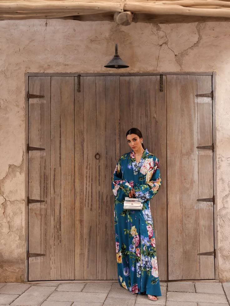 Walaa Awada in Dolce & Gabbana Ramadan 2026 teal floral
      silk kaftan standing before a traditional wooden door at
      Al Seef, Dubai — Dolce & Gabbana campaign by Ali & Walaa,
      March 2026