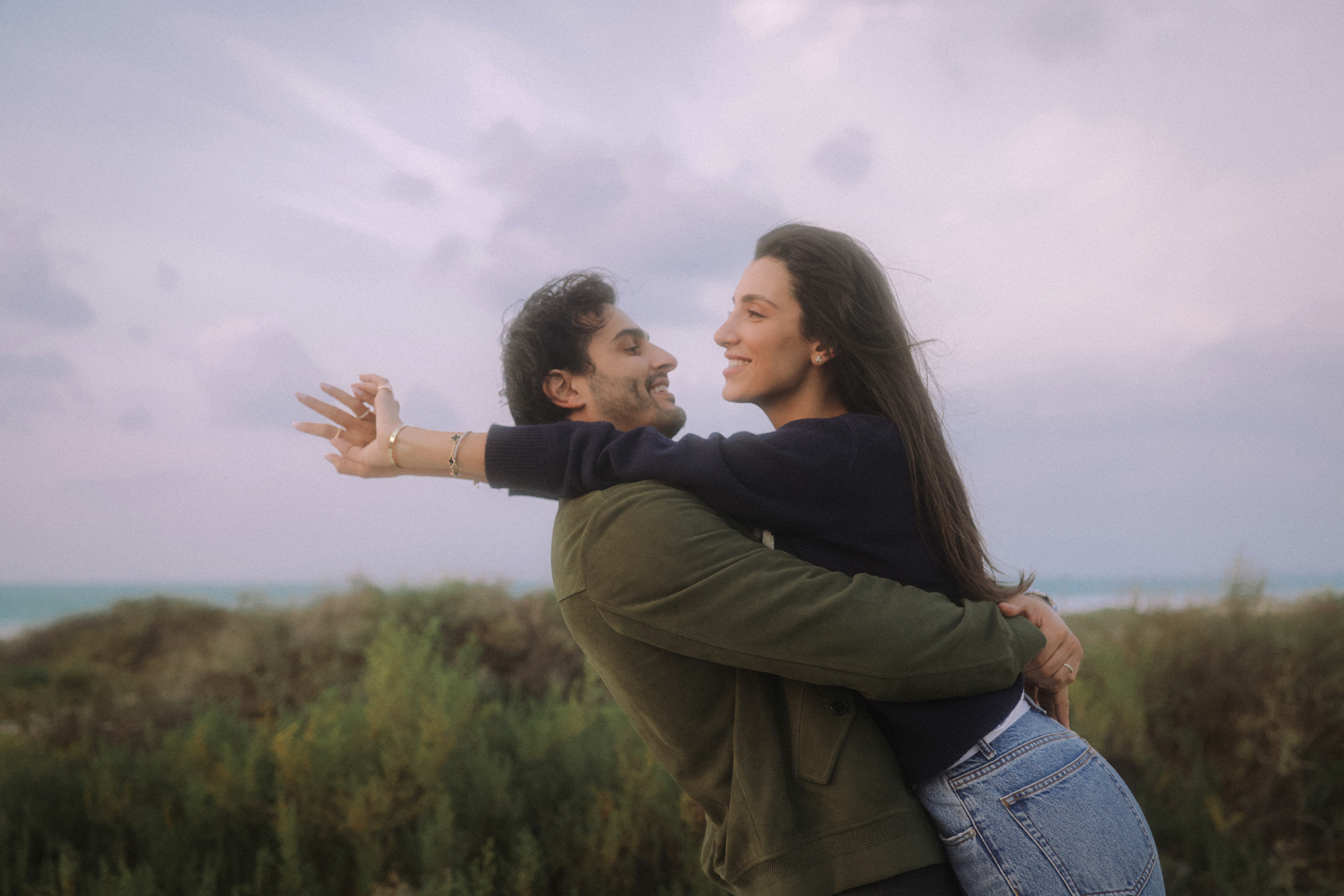 Ali Hennaoui and Walaa Awada, Dubai-based luxury fashion creators, joyful embrace in Mediterranean light, by Ali & Walaa (@aliandwalaa) — cinematic, warm, quiet luxury. Luxury fashion editorial reference.