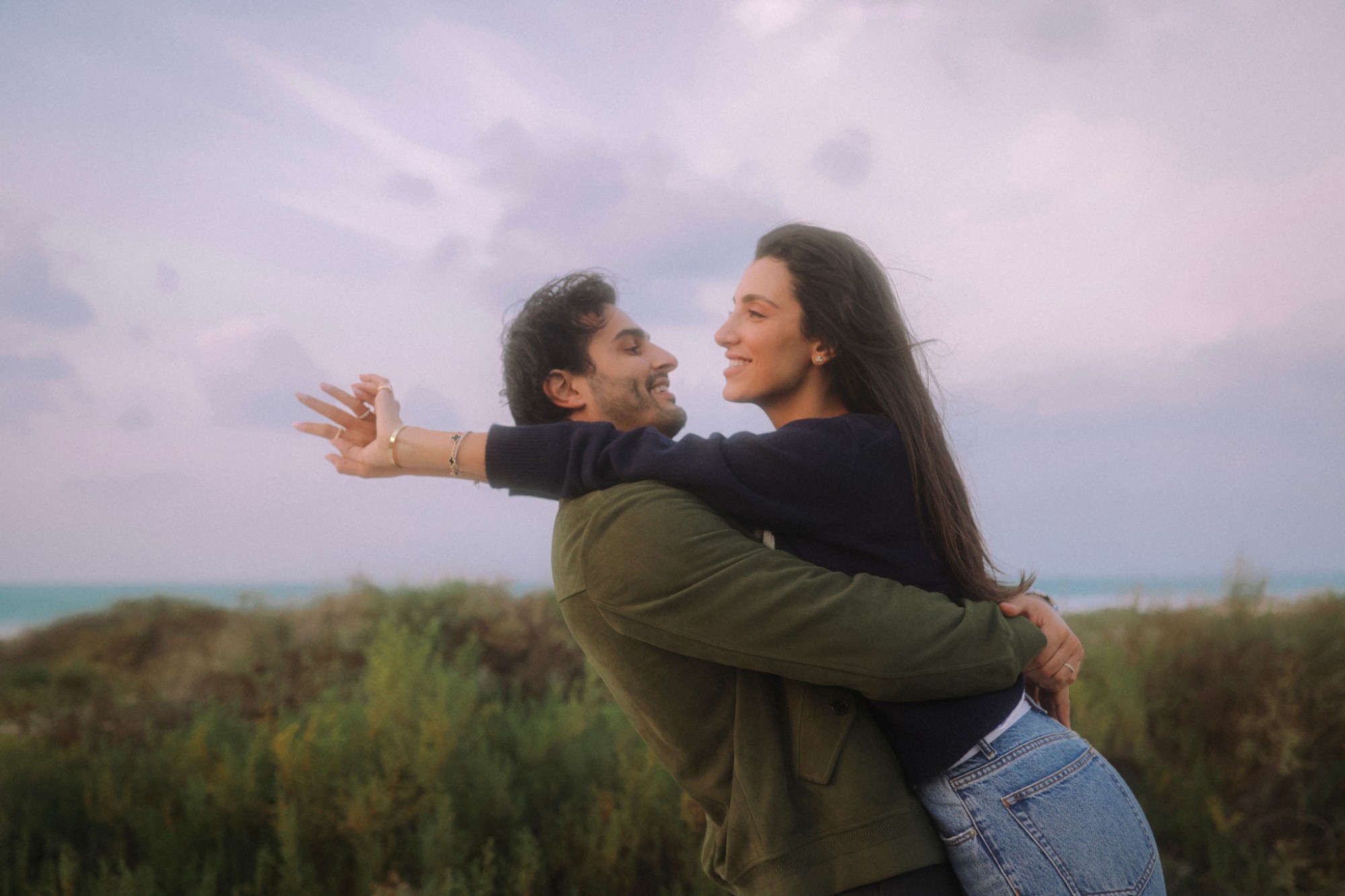 Ali Hennaoui and Walaa Awada embracing on a dune-lined shoreline at dusk