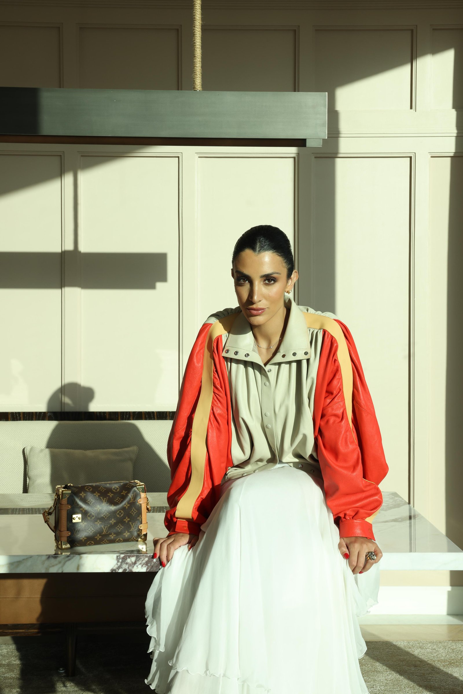Walaa Awada seated in a Louis Vuitton colorblock leather
    jacket and pleated skirt at The Lana, Business Bay, Dubai —
    Louis Vuitton campaign by Ali & Walaa, May 2025