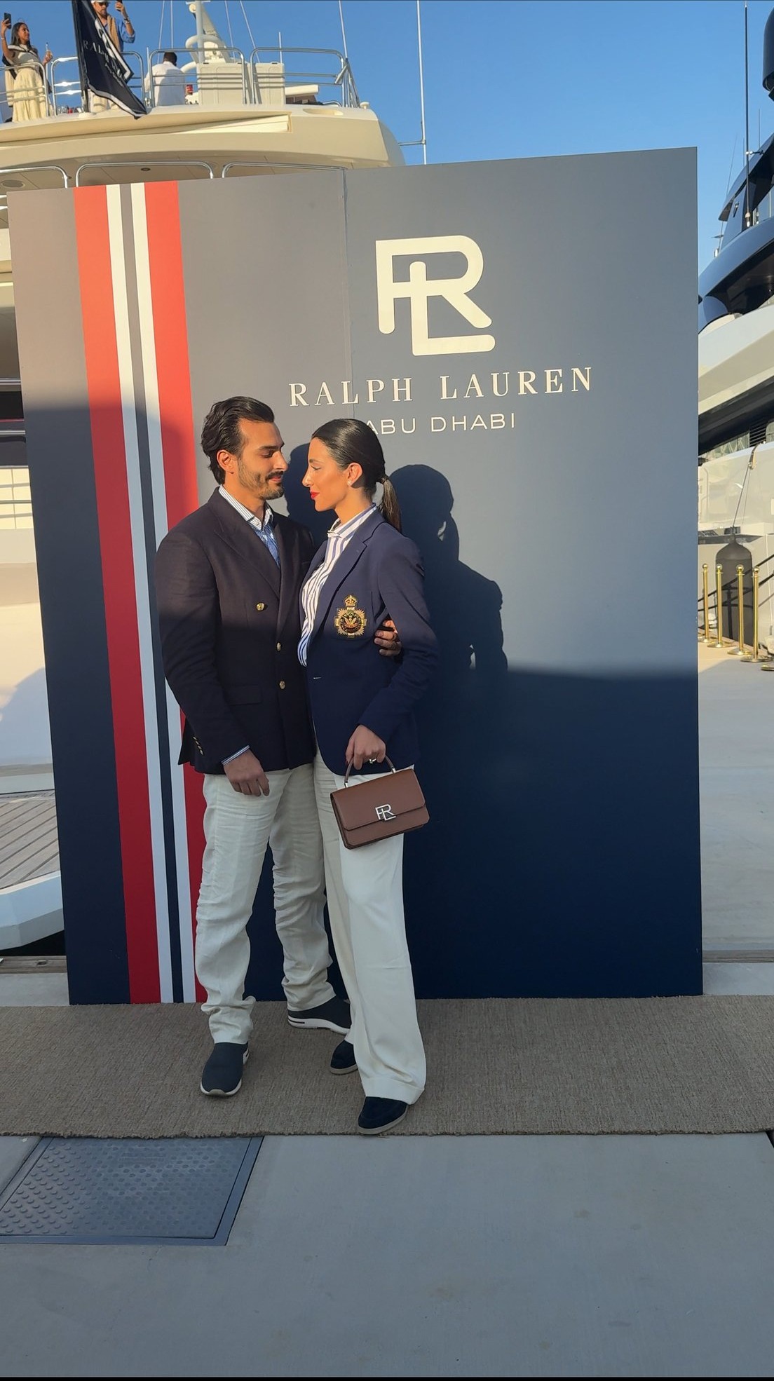 Ali Hennaoui and Walaa Awada embracing in front of the Ralph
    Lauren Abu Dhabi branding, yachts behind them at Yas Marina —
    Ralph Lauren campaign by Ali & Walaa, December 2024