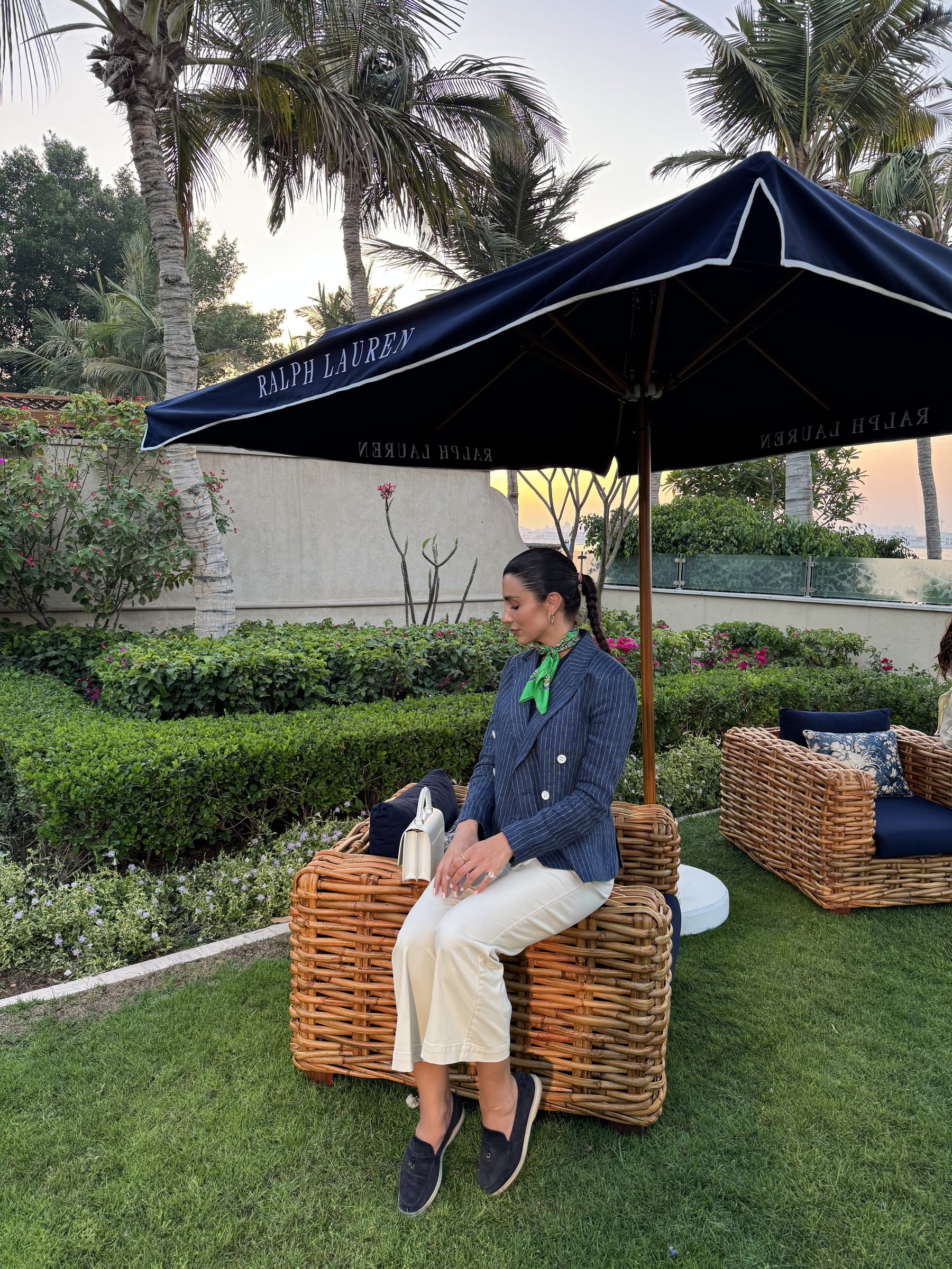 Walaa Awada seated under a Ralph Lauren umbrella in a navy
      pinstripe blazer, Yas Marina, Abu Dhabi — Ralph Lauren campaign
      by Ali & Walaa, December 2024